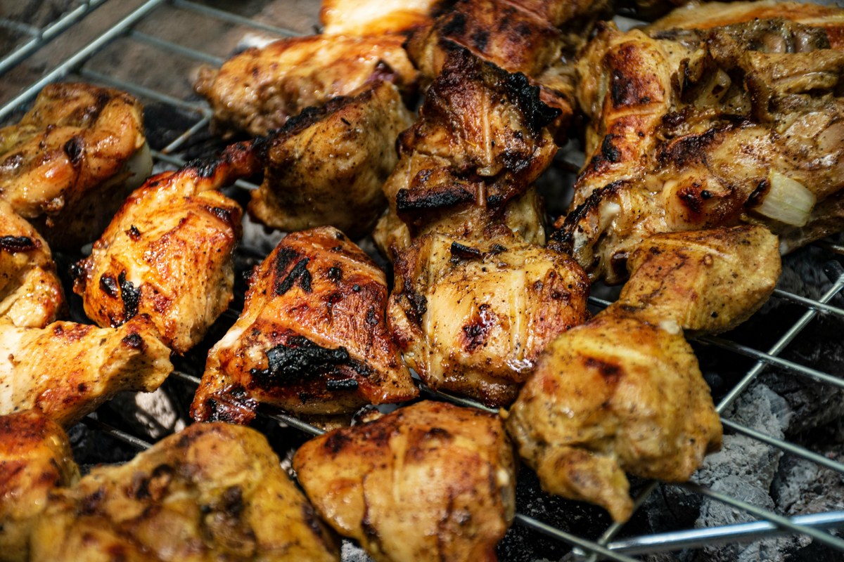 Charred spiced chicken tikka pieces on a grill rack.